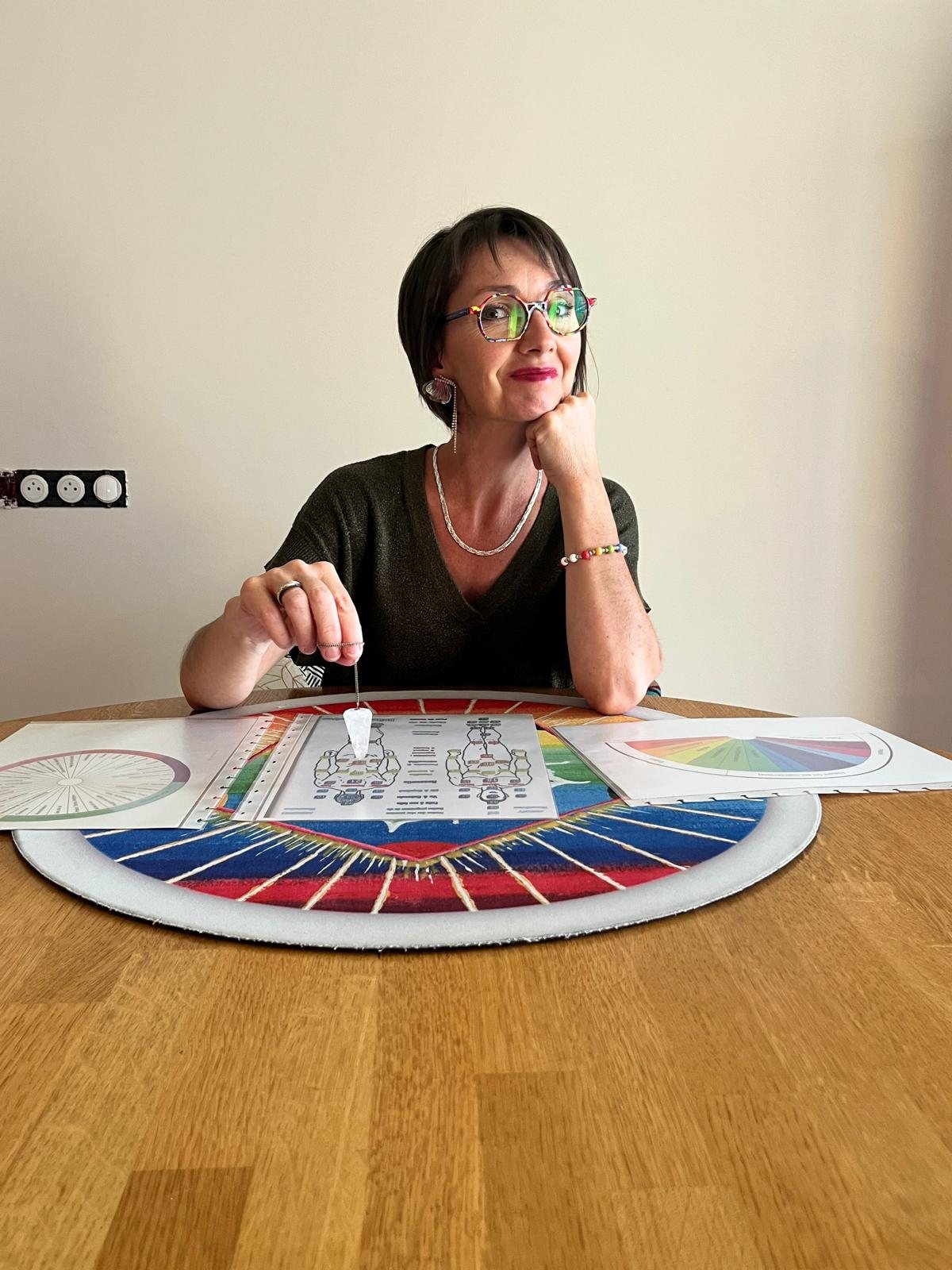 Émilie Haras à sa table de travail, un pendule au-dessus de son tapis peint